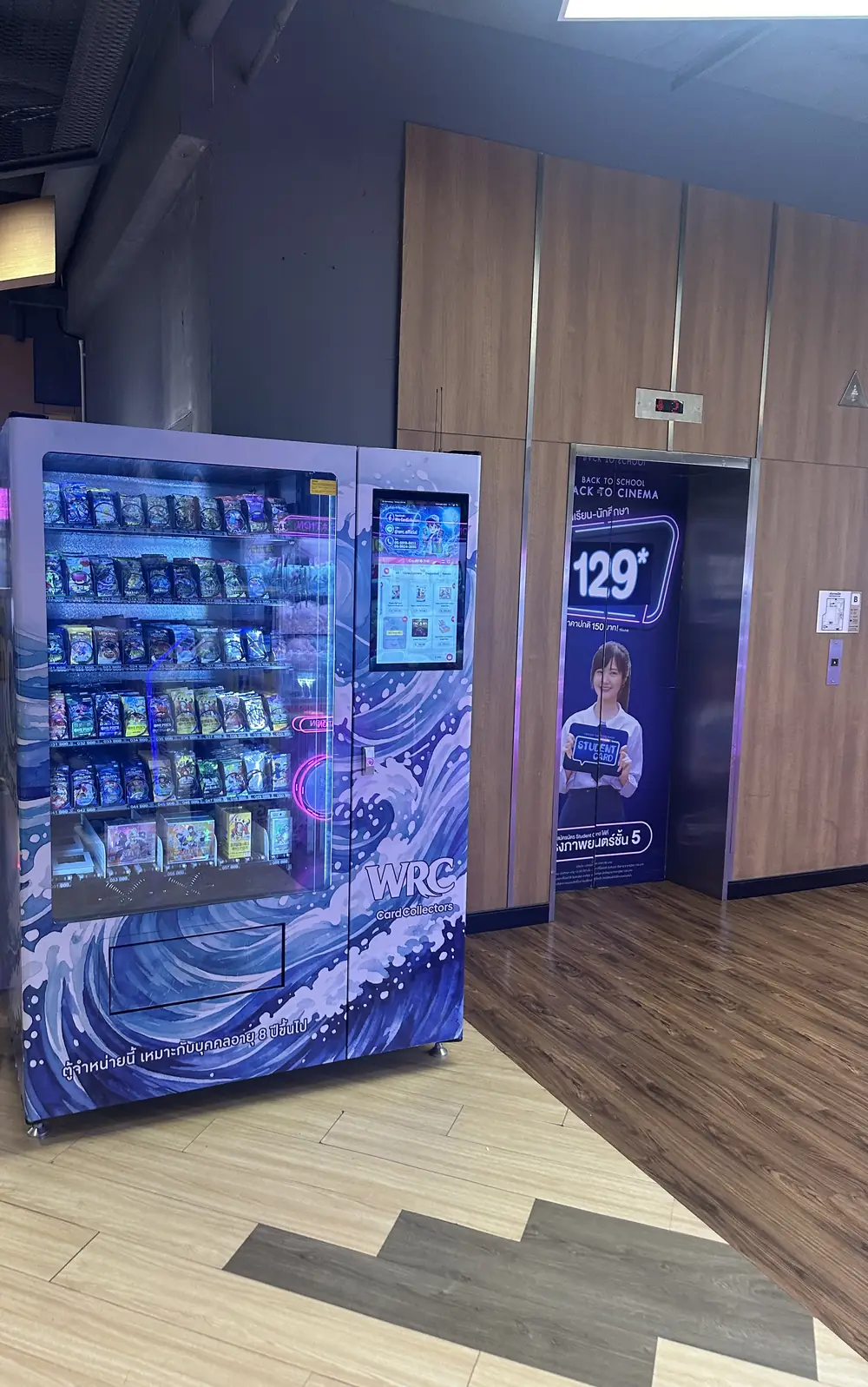 TCG-automat från operatören WRC CardCollectors placerad i en köpcentrumkorridor i Bangkok, med glasfront full av förseglade boosterpaket och en stående pekskärm på sidan
