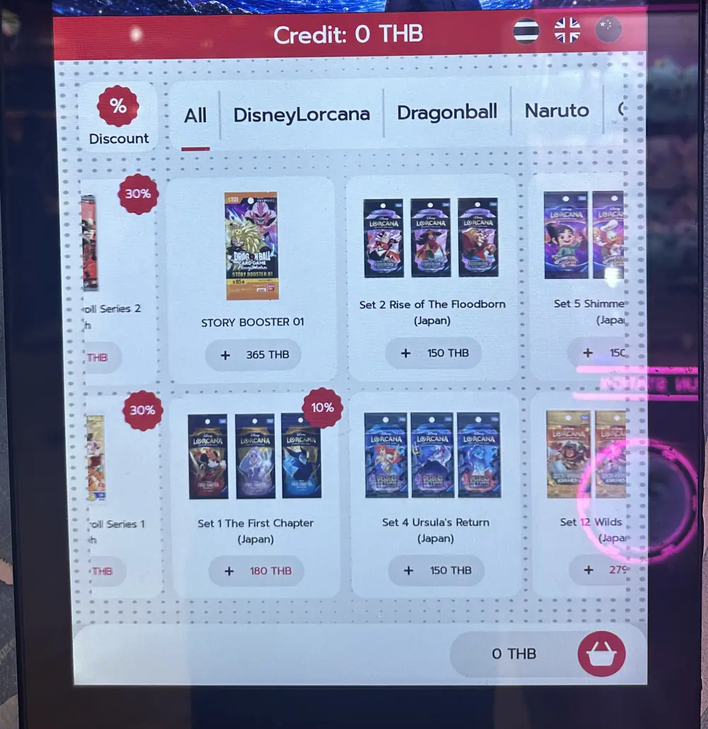 Pekskärmen på en TCG-automat i Bangkok som visar kategoriflikar för DisneyLorcana, Dragonball och Naruto med enskilda set, priser i thailändska baht och rabattmärkning